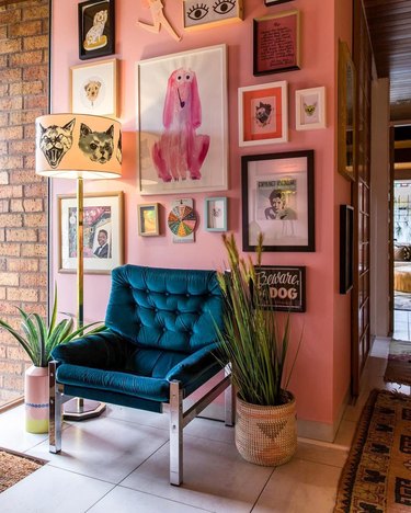Entryway with blue velvet chair, pink wall, floor lamp with cat shade, plants, art.