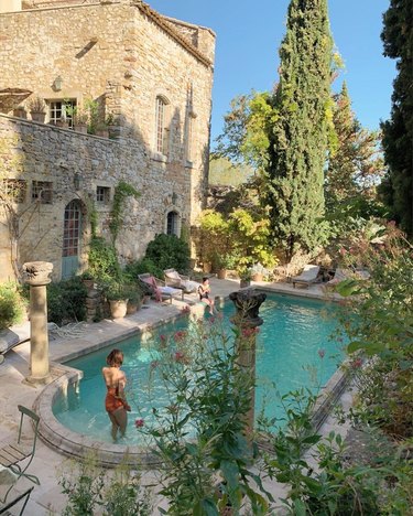 person in large pool near stone building with trees nearby