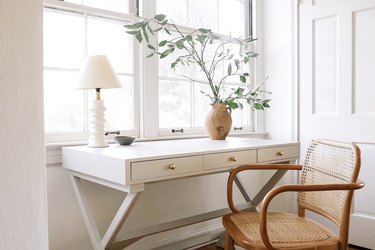 Home office desk painted with light gray milk paint in front of window with lamp and vase