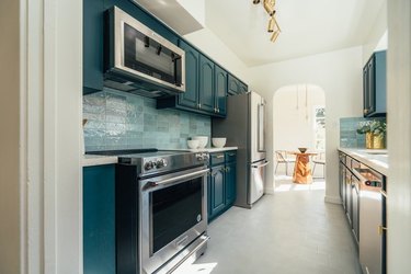 Kitchen with stainless steel electric stove, microwave, light blue subway tiles, sea blue cabinets.