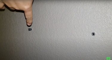 silver screws in white wall with finger pointing at one