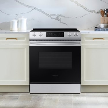 Kitchen with stainless steel electric stove, cream cabinets, marble backsplash.