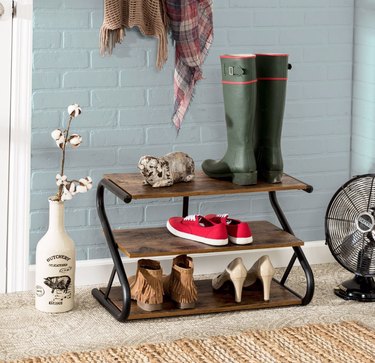 Rustic shoe organizer, rubber boots, shoes, fan, vase with dried flowers.