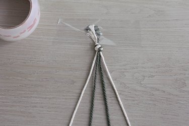 Four strands of cord tied into a knot and taped down to table