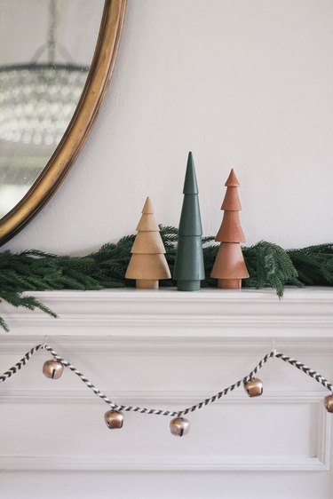 DIY sleigh bell garland hung under mantel decorated with wooden Christmas trees