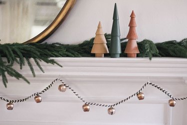 DIY sleigh bell garland hung under mantel decorated with wooden Christmas trees