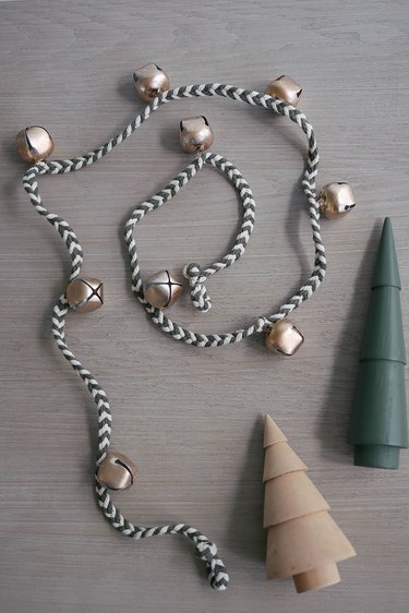 DIY jingle bell garland next to two wooden holiday trees