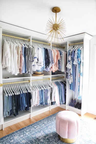Walk-in closet with white cabinetry and gold details, Sputnik chandelier, blue rug and pink ottoman.
