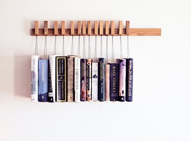 Wood book rack mounted on wall with books hanging from string
