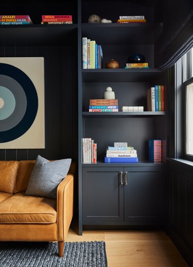 How To Organize a Bookshelf with Dark gray walls, leather couch, modern art, books, rug, wood floor.