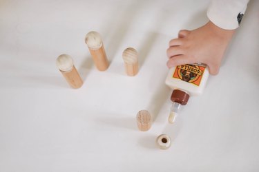 Gluing wood beads onto wood dowels to make dolls
