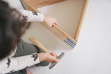Little boy hammering nail into dollhouse with tack hammer