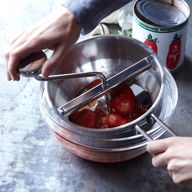 person using food mill with tomatoes