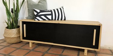 DIY storage bench in a black and wood finish with sleek handles and throw pillows