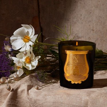 Balmoral candle next to a bouquet of flowers on a tan cloth.