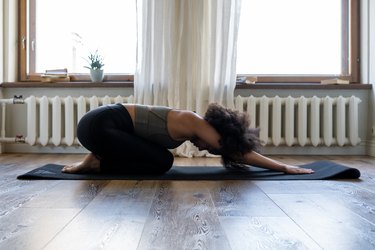 woman in child's pose on black yoga mat in front of bright windows