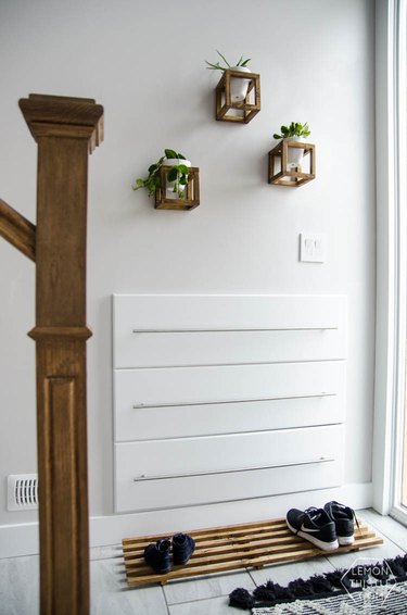 entryway shoe storage with minimalist wood mat in white entryway with hanging plants on wall