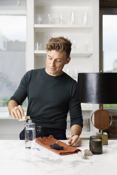 jeremiah brent pouring something into bottle in kitchen area with shelves in the background