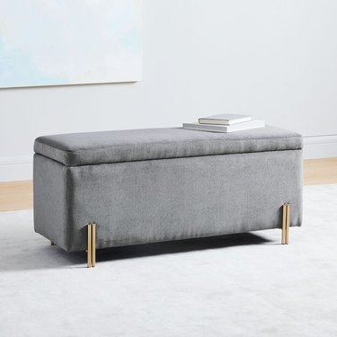 gray velvet cushioned bedroom storage bench with books on top