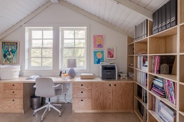 How To Organize a Bookshelf in room with desk, white arched ceiling, windows, desk chair, lamp, books, art.