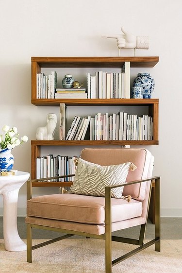 How To Organize a Bookshelf in room with rose upholstered and metal lounge chair, art, flowers, books.