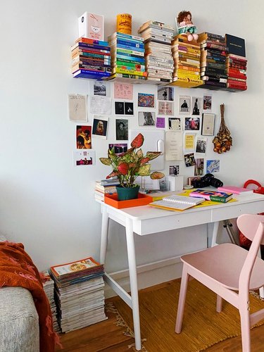 How To Organize a Bookshelf in Home office with white desk, pink chair, books stacked on shelf, art, plant.