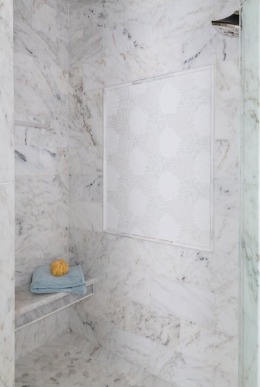 Marble tile in a shower with floral tile panel and bench