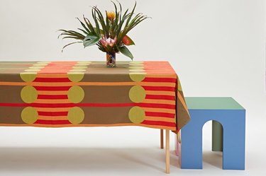 table with plant and colorful, patterned tablecloth, with blue stool nearby