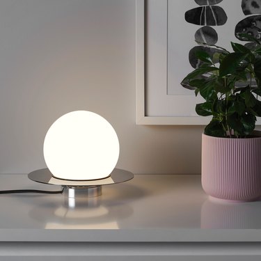 Simrishamn Table/Wall Lamp on white table with plant