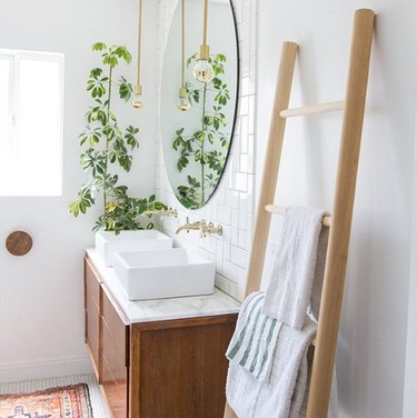 Bathroom with wood ladder towel rack, wood vanity, vessel sinks, plant, round mirror and Scandinavian Bathroom Storage Ideas