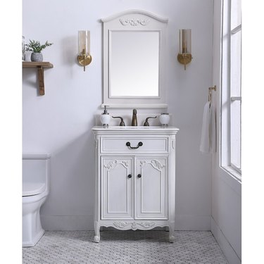 French country bathroom sink with white vintage style vanity with matching mirror, sconces, hexagon tile floors, toilet, towel.