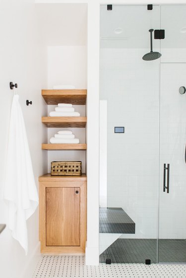 white bathroom with wooden built-in bathroom shelving and a glass door shower