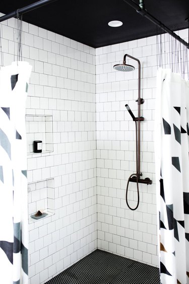 Corner shower with white tile walls and black and white shower curtains