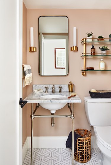 pink powder room with glass bathroom shelving above the toilet and next to a vanity mirror