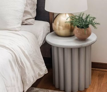 Ribbed side table with plant next to bed