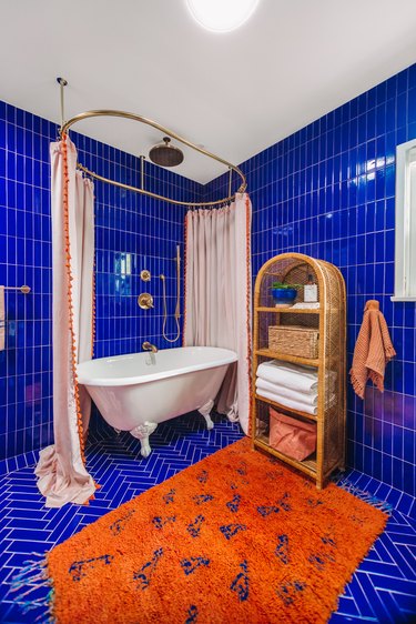 Floor to ceiling blue shower tile in modern bathroom with orange rug