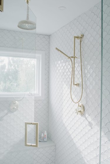 Coastal shower with white fish-scale tiles and gold fixtures