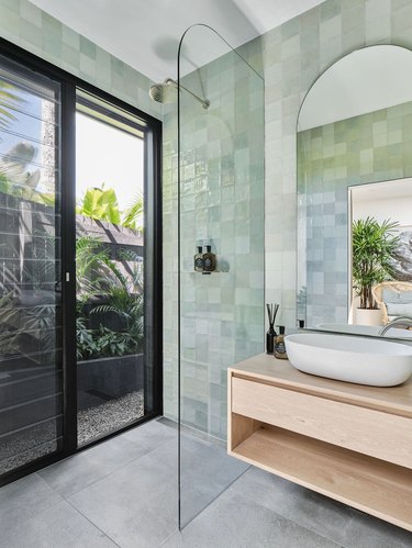 Green tile shower in light green with window overlooking tropical landscaping