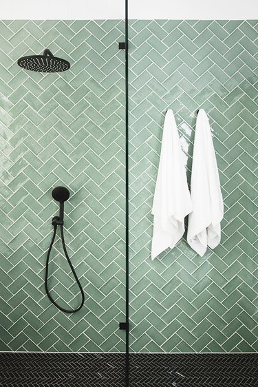 Green tile shower in mint green with black fixtures in a herringbone pattern