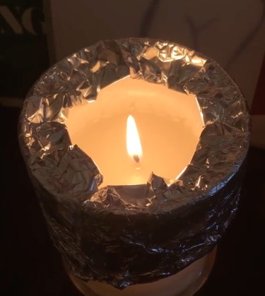 burning candle with tin foil around edge of jar
