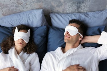 two people in bed wearing eye masks and bathrobes