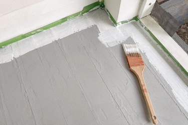 Painting primer along baseboards with paintbrush