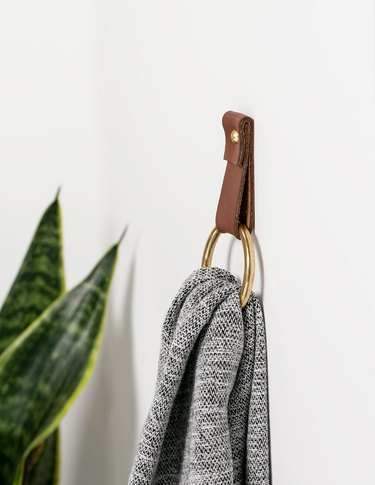 Leather and brass towel rack for small bathroom with gray towel and houseplant