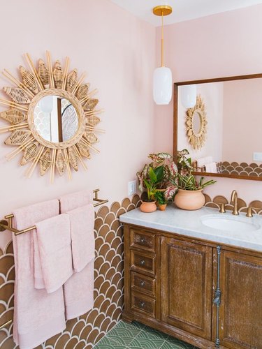 small boho bathroom with pink wall and brown backsplash and sunburst mirror