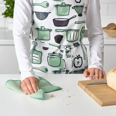person with apron holding green dish cloth near cutting board with bread