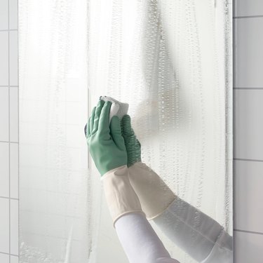 person with green gloves cleaning mirror