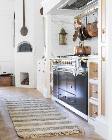 white french country style kitchen with black stove and a rug, copper pots hanging above