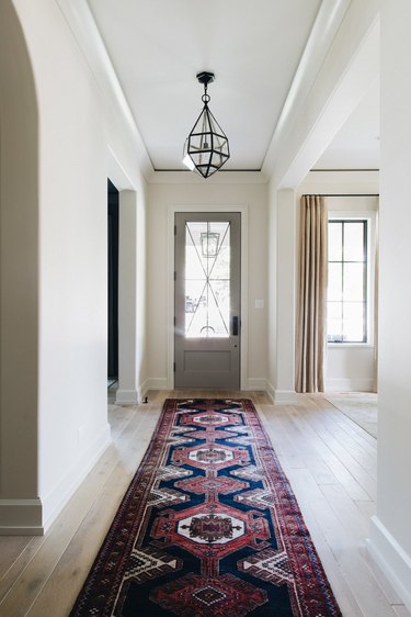 Entryway with glass pendant lamp, Oriental runner rug, wood floors.