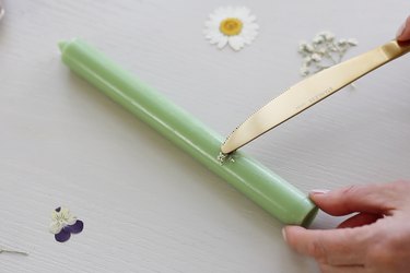 Pressing hot knife on top of pressed flower to melt into green taper candle