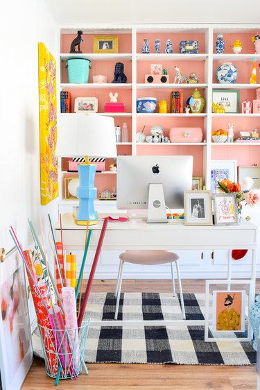 white home office with pink painted bookcase behind a white office desk, checkered rug
